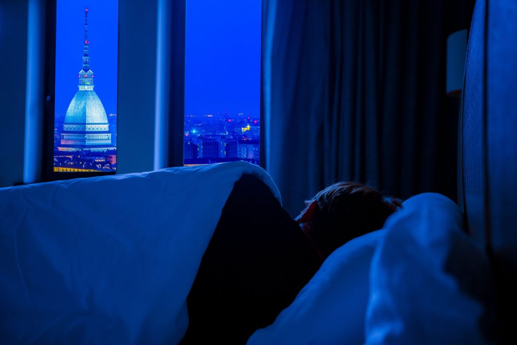 Il sonno come alleato del benessere: perché dormire bene è così importante A serene view of Turin's night skyline featuring Mole Antonelliana, seen from a cozy bedroom.