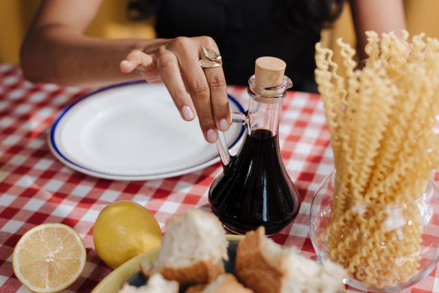 Aceto balsamico: tradizionale DOP contro IGP A close-up of a hand reaching for vinegar at an Italian-themed table.