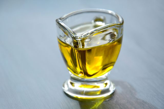 Olio extravergine d'oliva: origini, storia e come riconoscerne uno buono A close-up photo of a small glass jug containing yellow liquid against a white background.