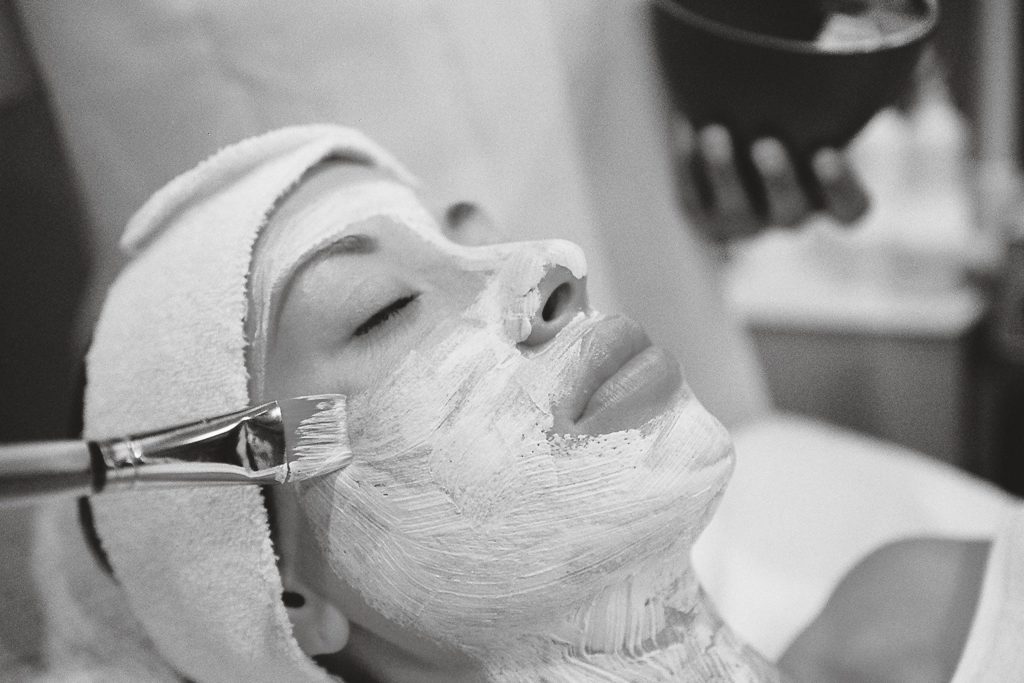 Detox viso di stagione: la routine per una pelle luminosa A serene spa scene with a woman receiving a facial mask treatment.