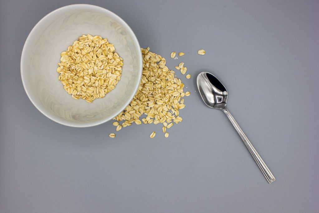 Barrette Proteiche Naturali Avena & Frutta Secca Minimalist top view of oats in bowl with a spoon on gray background.