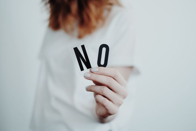 Imparare a dire di no: proteggere tempo ed energie, al lavoro e a casa Close-up of a person holding a "No" sign, symbolizing rejection or disagreement.